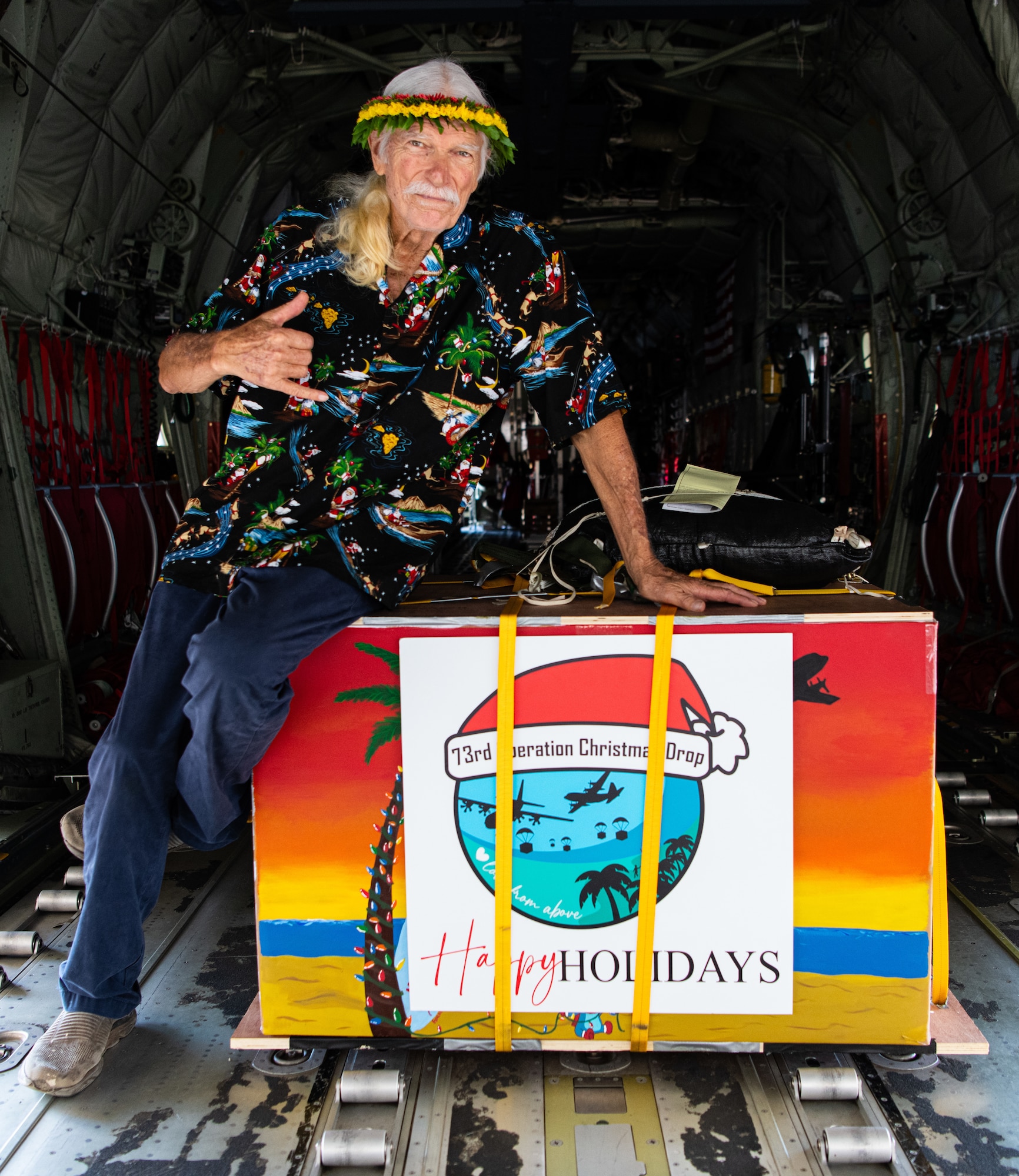 Bruce Best, known as “Brother Bruce,” Operation Christmas Drop  island liaison and coordinator, sits on a humanitarian-like aid bundle in the cargo hold of a U.S. Air Force C-130J Super Hercules aircraft from the 374th Airlift Wing in Yokota, Japan, during the Operation Christmas Drop 2024 “Push Ceremony” at Andersen Air Force Base, Guam, Dec. 9, 2024.