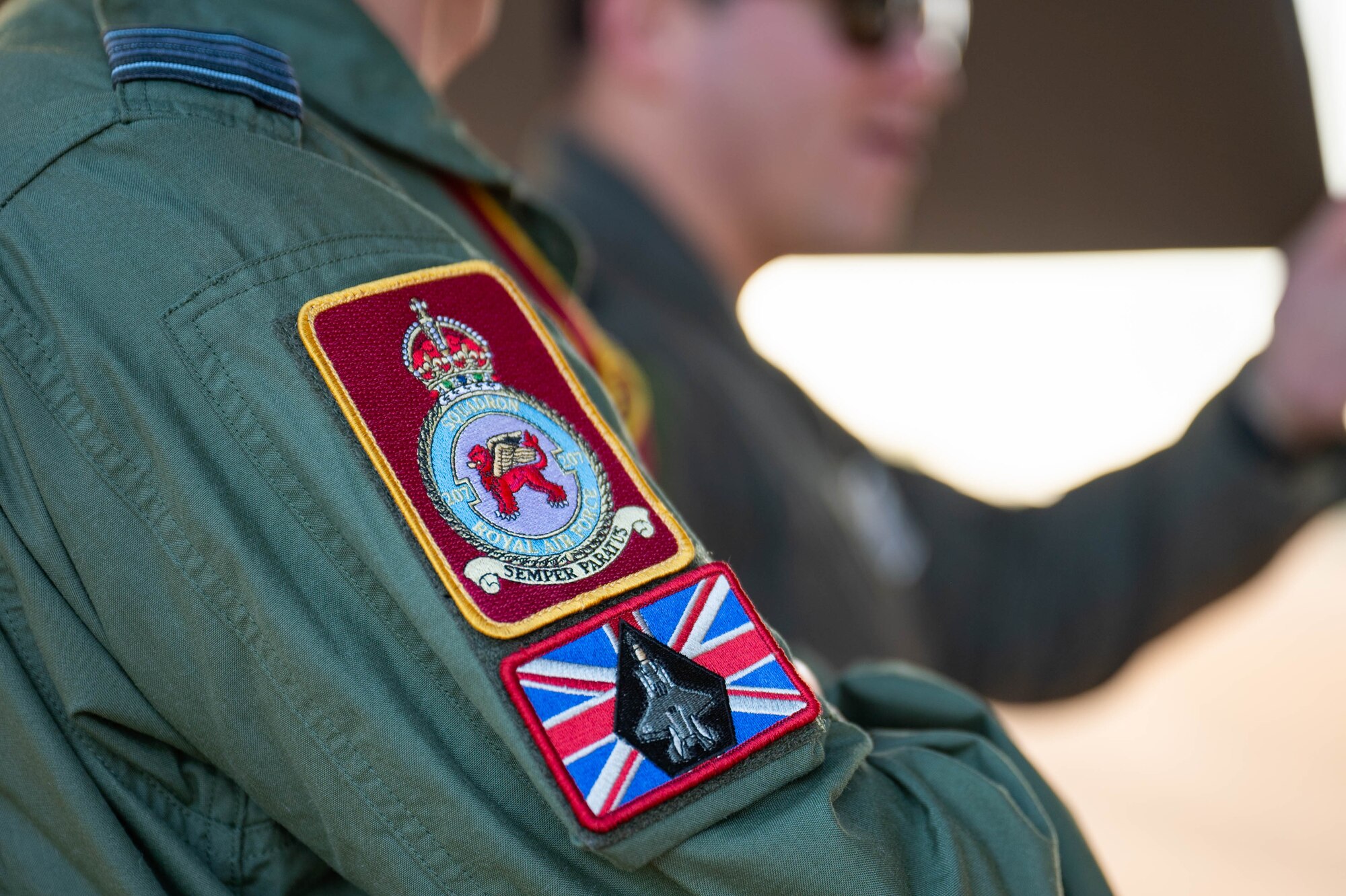 A member of the Royal Air Force speaks to a U.S. Air Force Airman during Bomber Task Force 25-1, at RAF Fairford, England, Nov. 13, 2024. The patches shown represent the 207 Squadron, which is the F-35 Lightning Operational Conversion Unit located at RAF Marham. (U.S. Air Force photo by Senior Airman Mary Bowers)