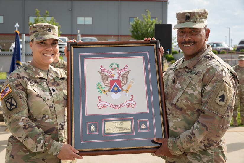 Command Sgt. Maj. Robert C. Render, 103rd Brigade Support Battalion, is presented the unit's coat of arms from Lt. Col. Esther Platt at his retirement ceremony in Harrodsburg, Kentucky on June 14, 2024. Render is retiring from the Kentucky Army National Guard with 43 years, and 10 months; he is longest serving member of the Kentucky National Guard. (U.S. Army National Guard photo by Sgt. 1st Class Andrew Dickson)