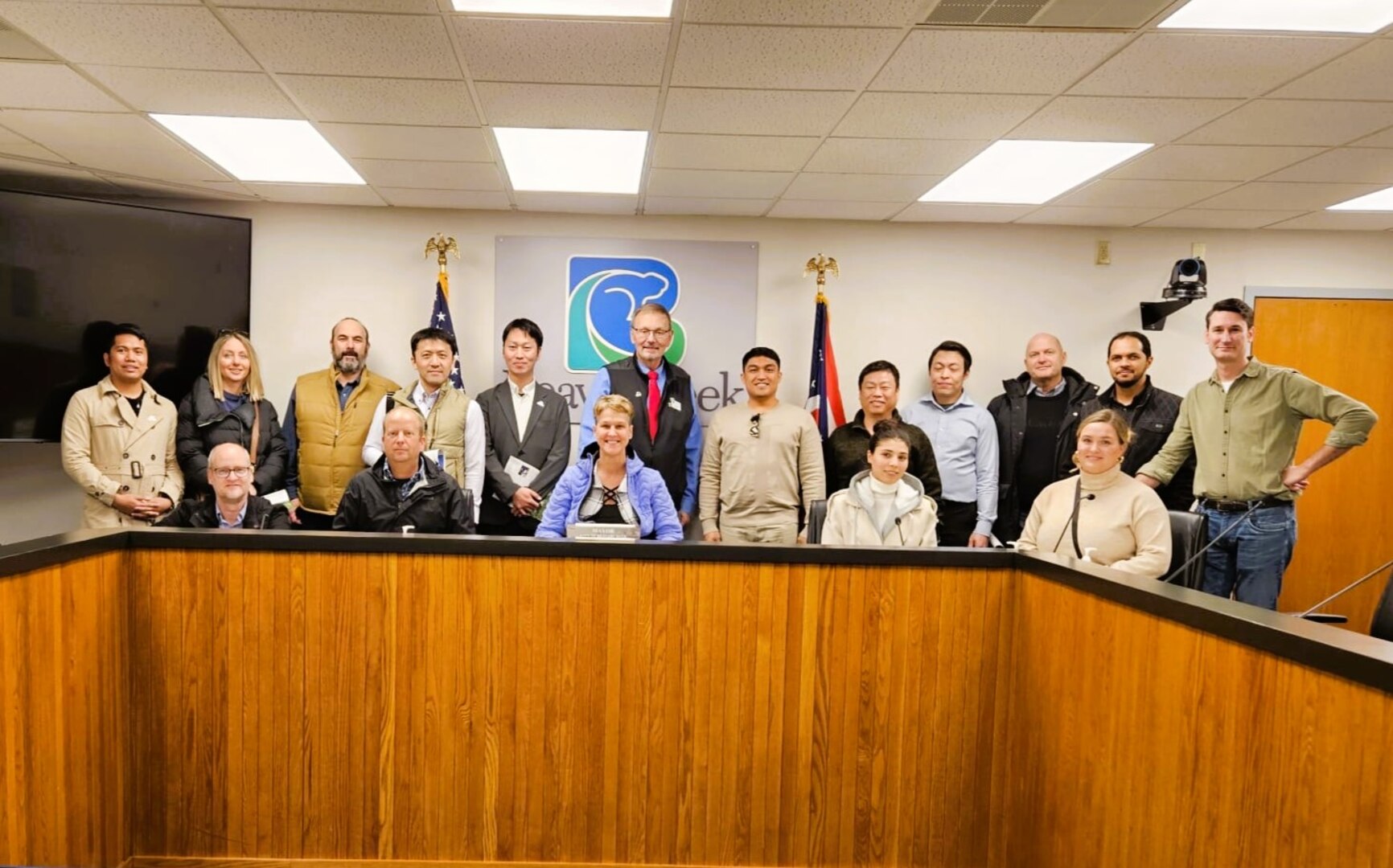 17 adult students stand behind a desk