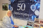Ms. Stokesbury poses in front of a 50 years sign and prepares to cut celebratory cake