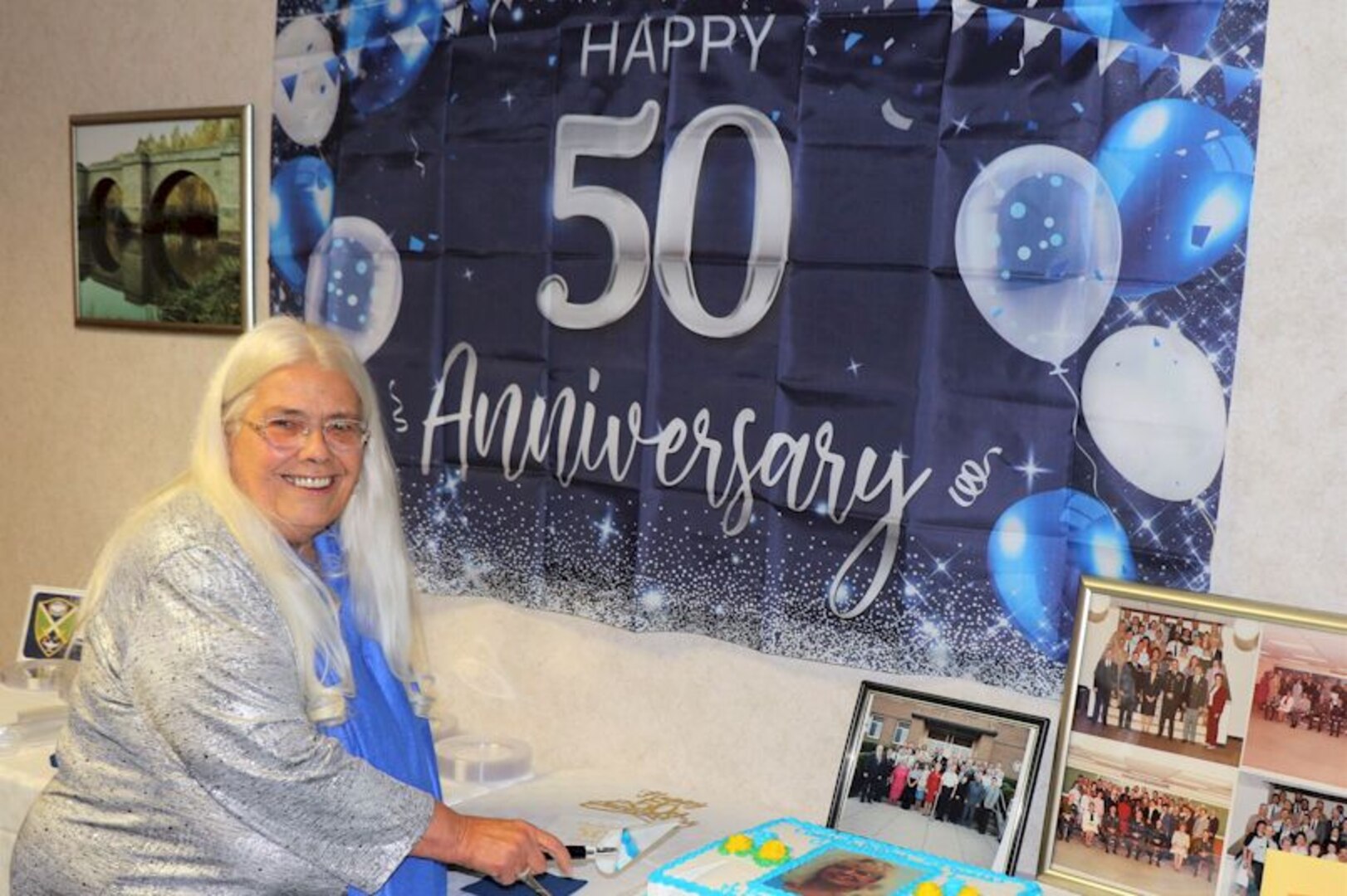 Ms. Stokesbury poses in front of a 50 years sign and prepares to cut celebratory cake