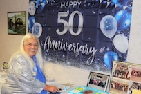 Ms. Stokesbury poses in front of a 50 years sign and prepares to cut celebratory cake