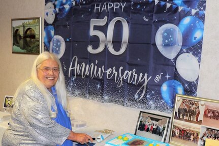 Ms. Stokesbury poses in front of a 50 years sign and prepares to cut celebratory cake