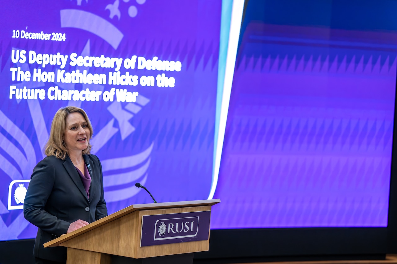 A woman speaks from behind a lectern in front of a screen.
