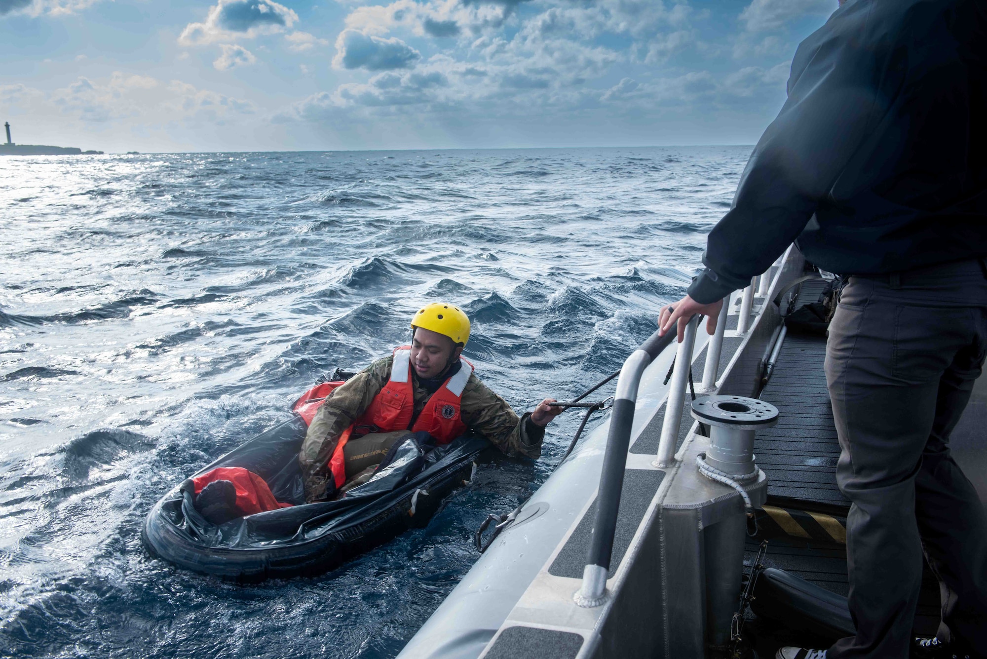 Service member sits on a raft in the ocean.
