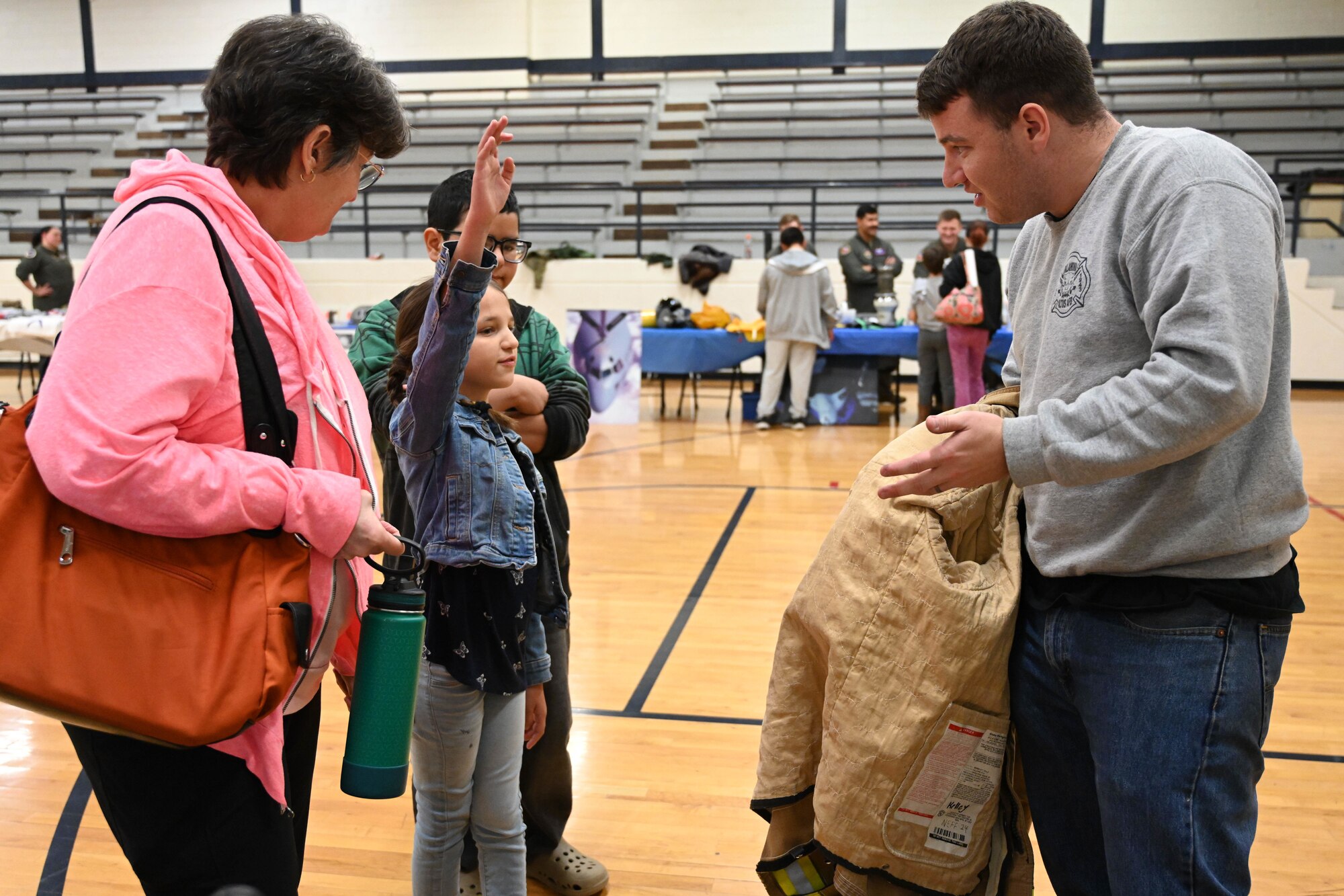 U.S. Air Force Staff Sgt. Thomas Reno, 97th Civil Engineer Squadron lead firefighter (right), shows bunker gear to Juniper and Jaydon, Aviation Inspiration and Mentorship Fair participants, at Altus Junior High School in Altus, Oklahoma, Dec. 7, 2024. Bunker gear is the protective clothing and equipment that firefighters wear to protect themselves from flames. (U.S. Air Force photo by Senior Airman Miyah Gray)