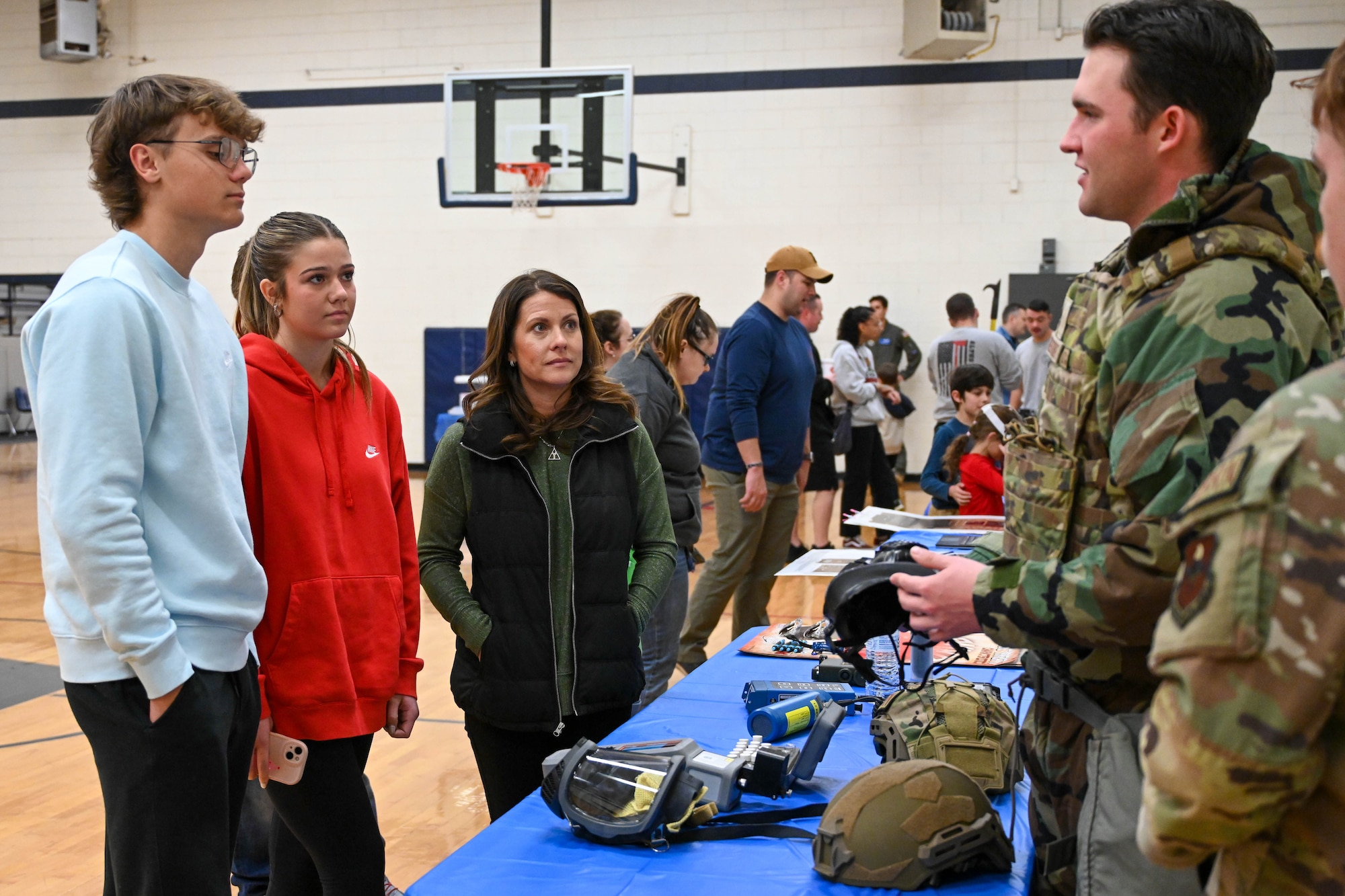 U.S. Air Force Airman Corin Armentrout, 97th Civil Engineer Squadron emergency management apprentice, explains Raman spectroscopy to Brenna Marshall, 97th Air Mobility Wing commander’s wife (right), and Maggie and Griffin Marshall at an Aviation Inspiration and Mentorship fair at Altus Junior High School in Altus, Oklahoma, Dec. 7, 2024.  Raman spectroscopy is a non-destructive chemical analysis based on an object’s interaction with light. (U.S. Air Force photo by Senior Airman Miyah Gray)