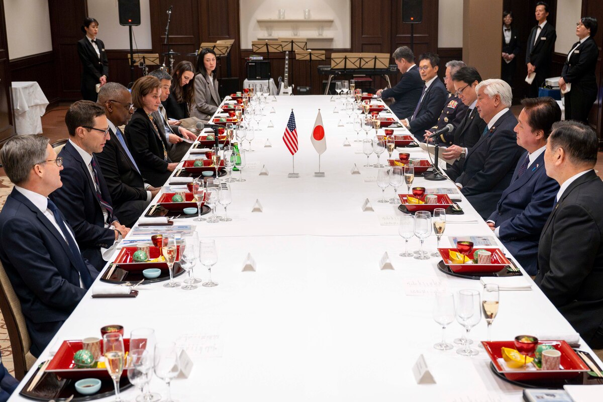 A group of people sit at a long table. Food and drinks are on the table.
