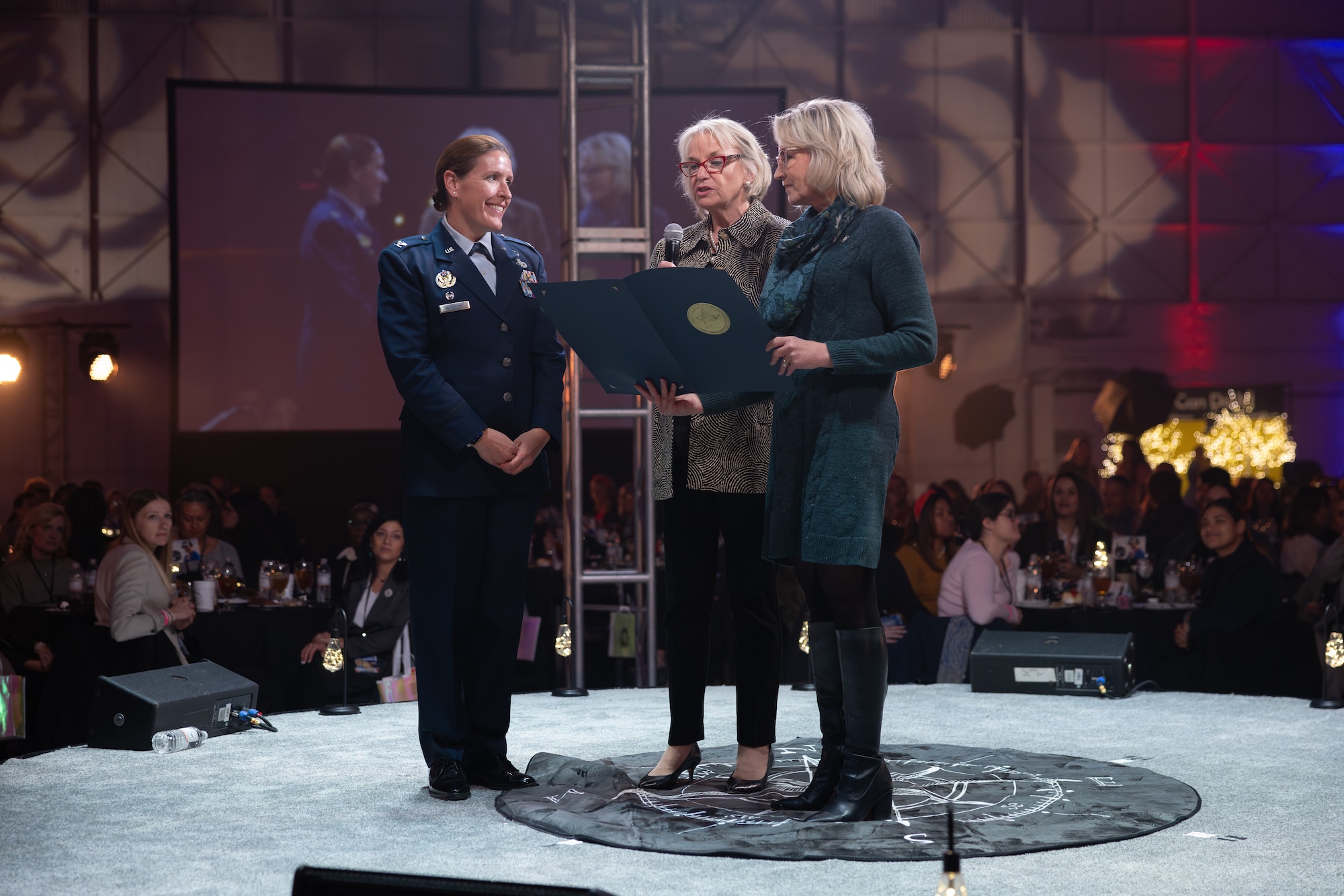 Woman receiving award from two other women on stage in front of audience.