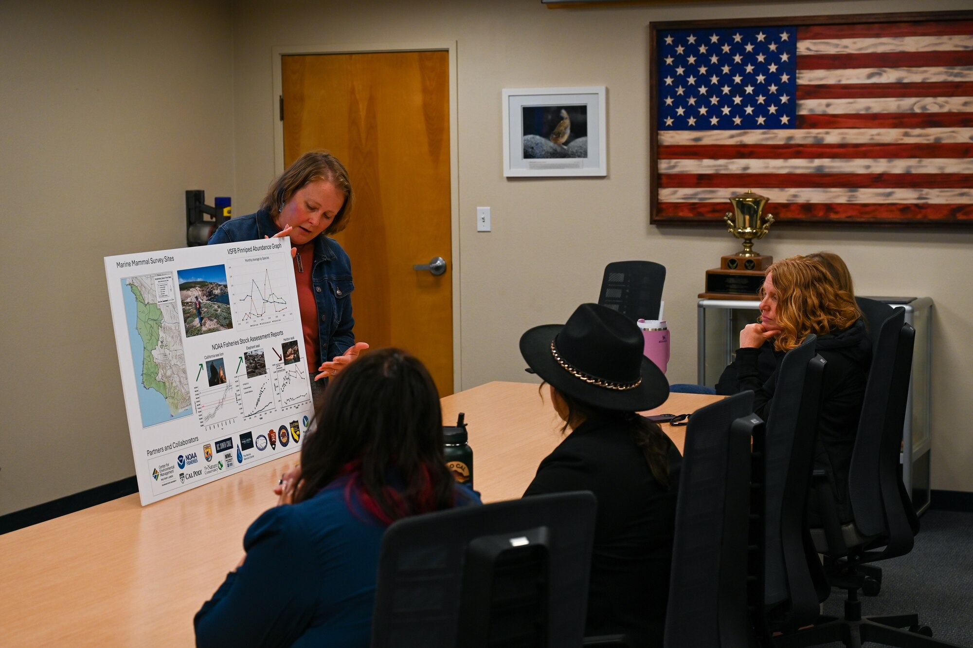 A group of people sit at a table watching a presenter.