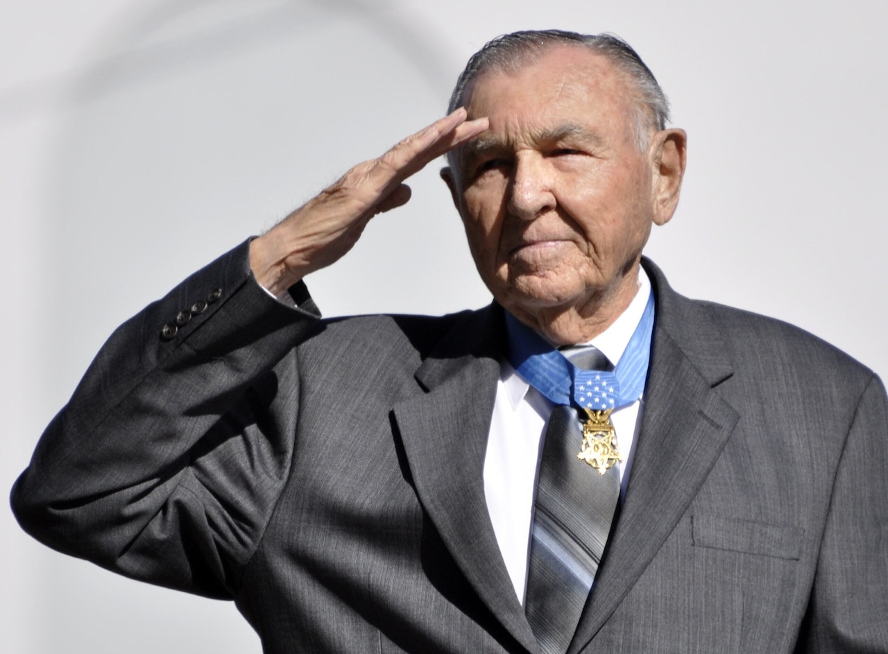 A man wearing a medal around his neck salutes.