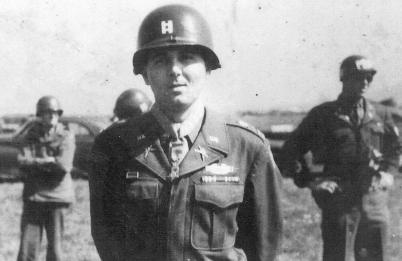 A man in uniform and metal helmet stands at attention while wearing a medal around his neck.