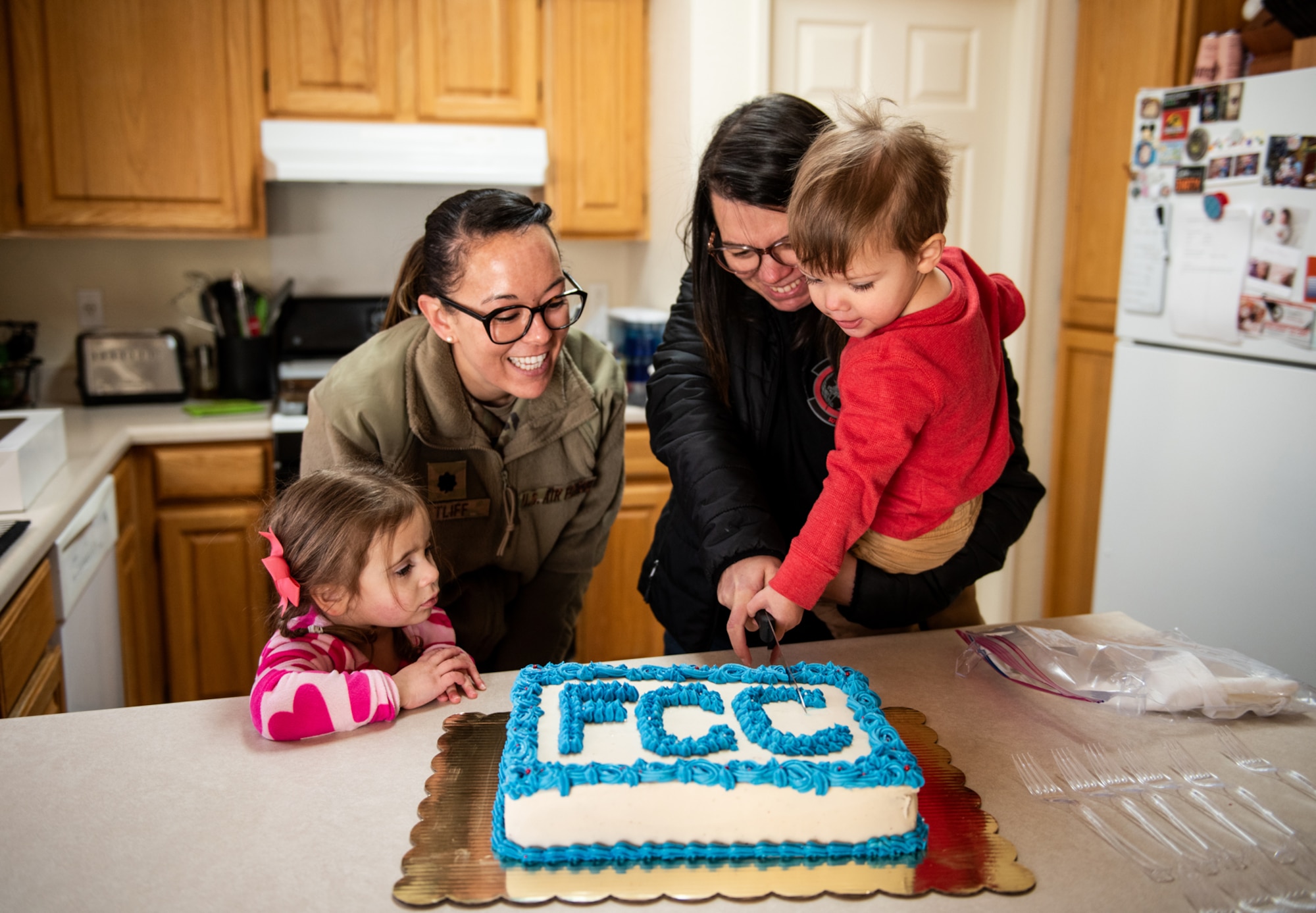 Military member, civilian woman, and two children cut FCC cake in a kitchen