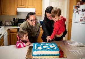 Military member, civilian woman, and two children cut FCC cake in a kitchen