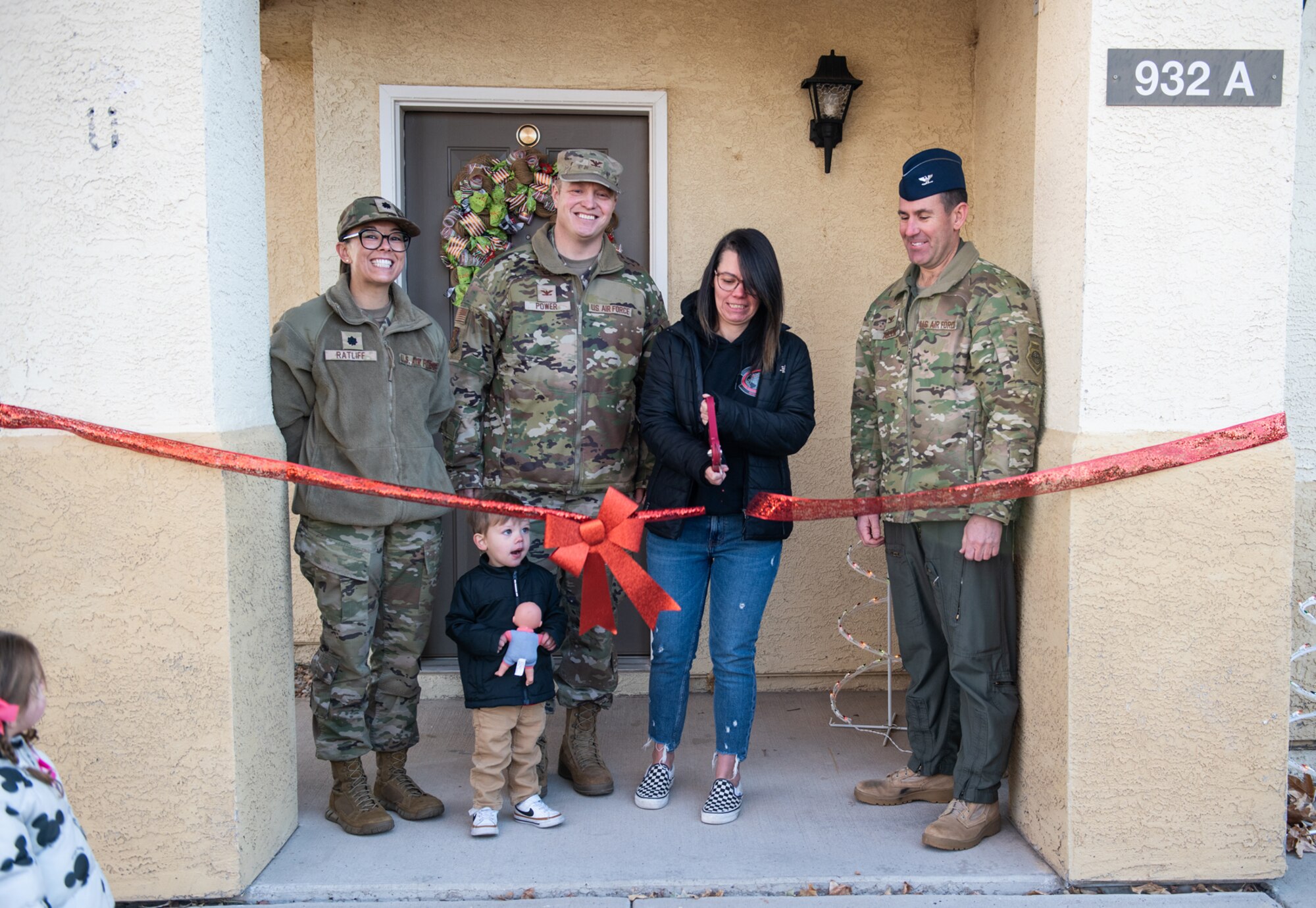 Military members watch as a civilian woman cuts the ribbon in front of her home as a new childcare provider