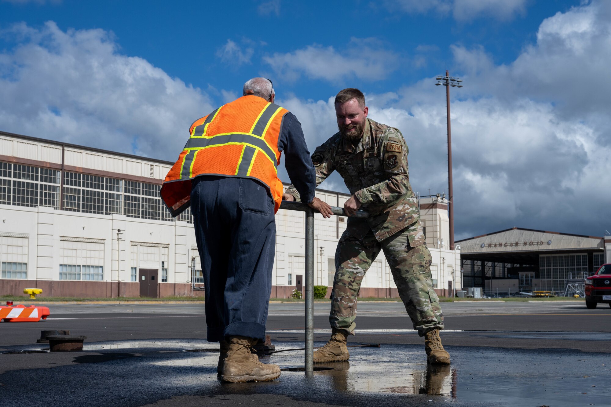 Two men utilize equipment while working on hardware under the concrete on the flightline.