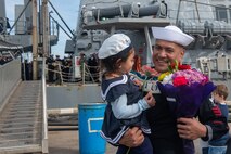A U.S. Navy Sailor assigned to Arleigh-Burke class guided-missile destroyer USS Arleigh Burke (DDG 51) poses with their child at Naval Station (NAVSTA)