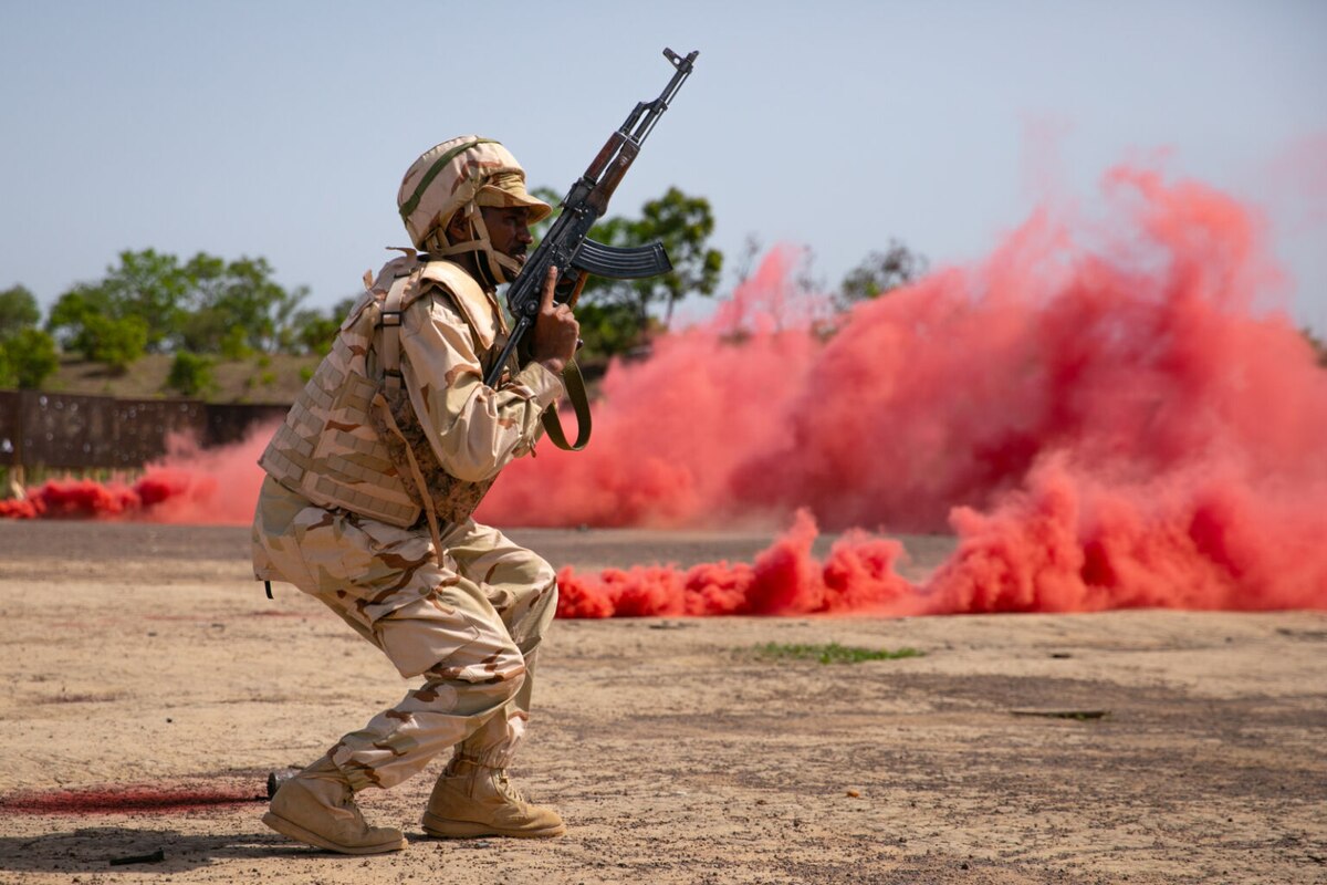 A soldier advances as a smoke grenade spews red smoke.