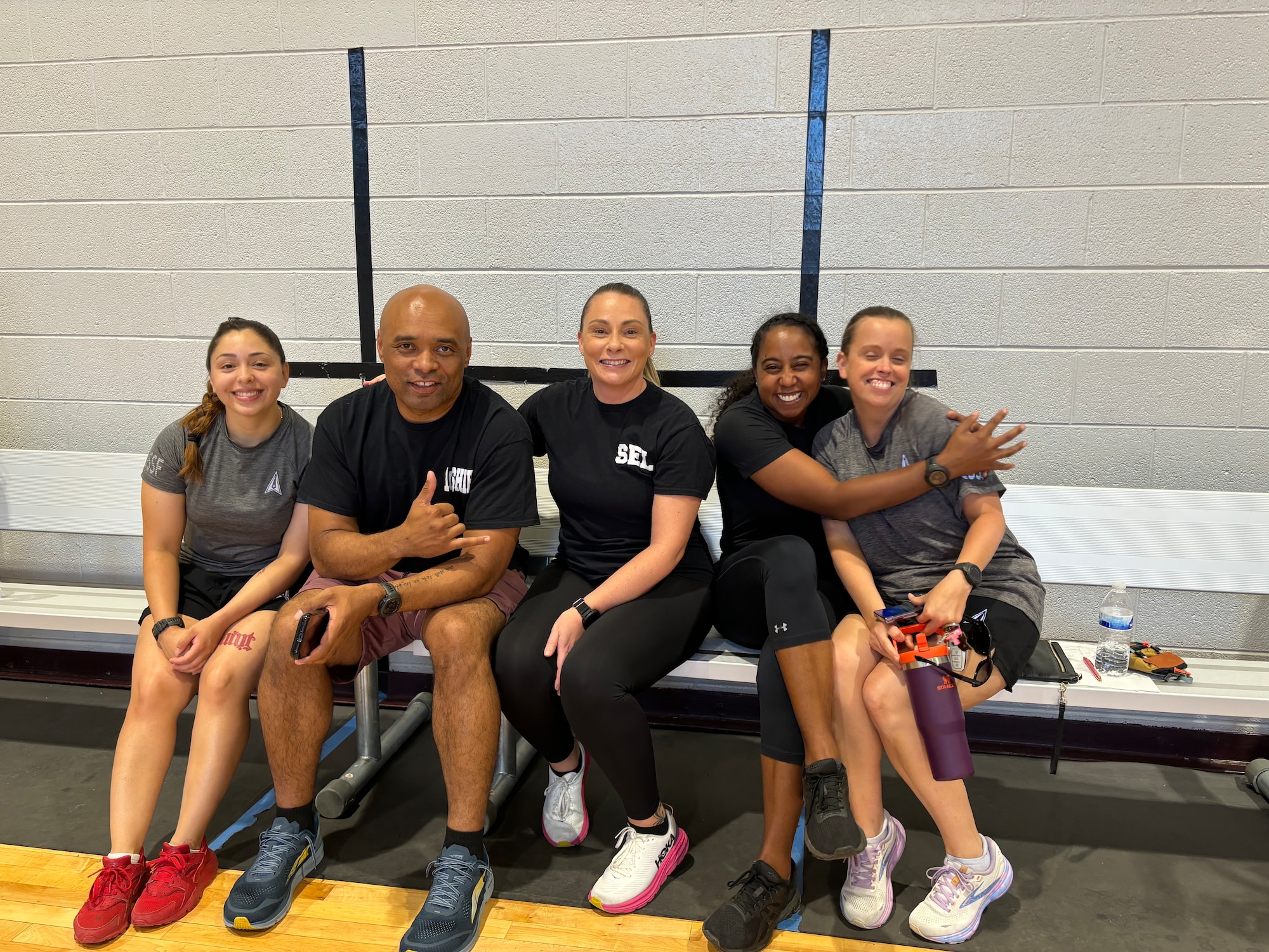 Military members sit on a bunch in a gym.