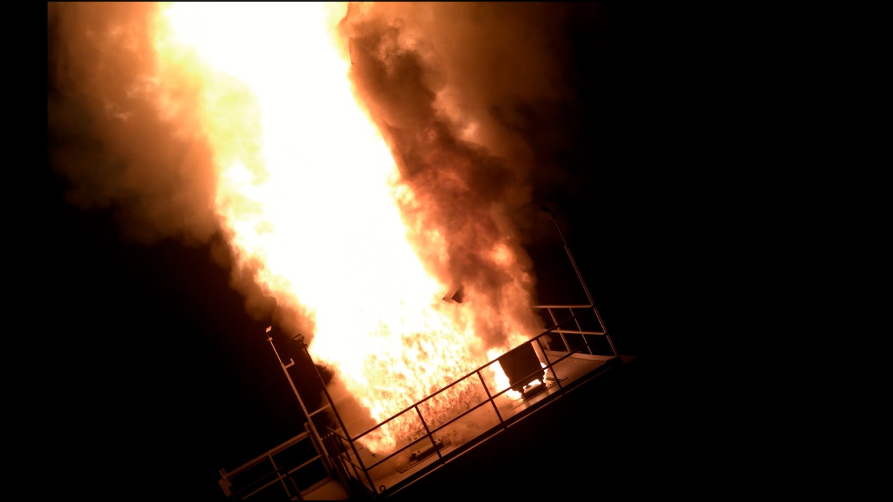 Bright flames are shooting upward out of a launching device at night.