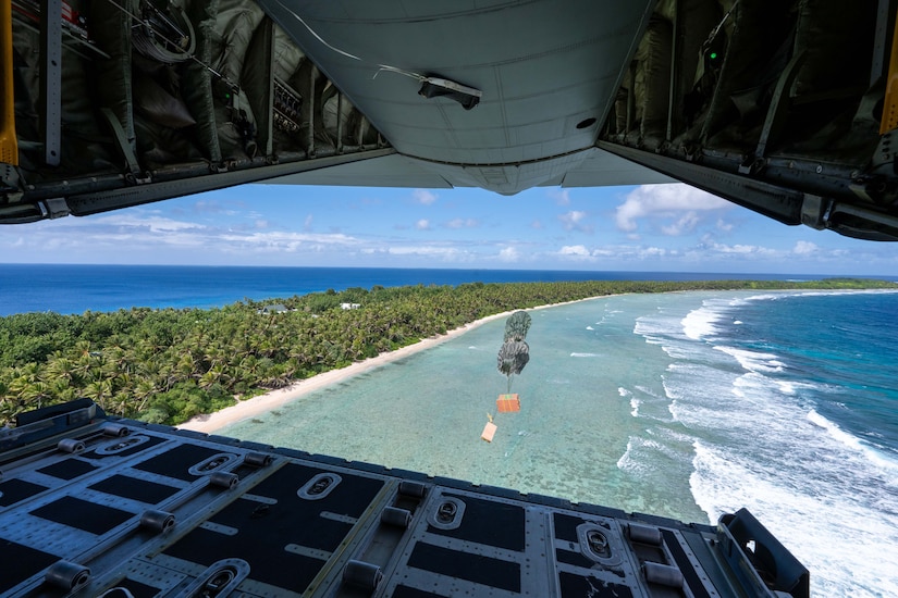 Two boxes of supplies drop over the sea next to land.