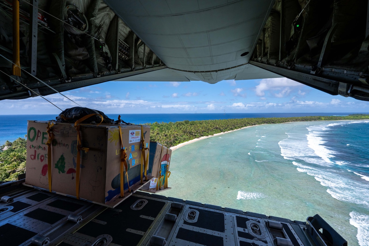 Two boxes of supplies drop from the back of an open aircraft to the sea.