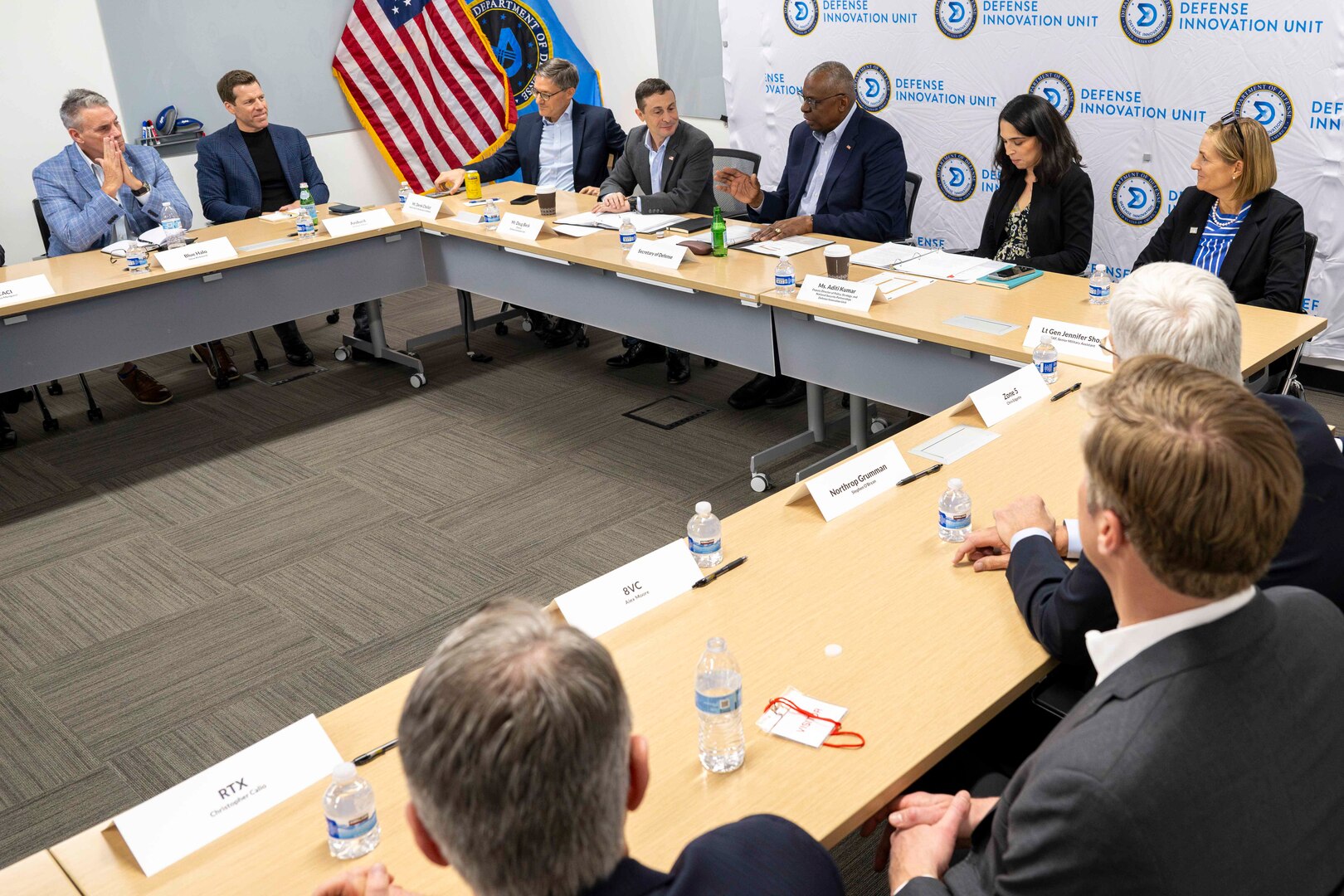 Men and women in civilian attire are seated at tables.