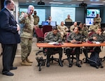 Soldiers sit in a classroom setting with screens in the background