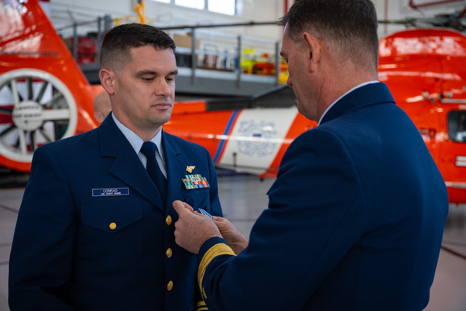 Rear Adm. Joseph Buzzella (right) pins the Distinguished Flying Cross Medal on Lt. Cmdr. Jacob Conrad during an award ceremony at Air Station San Francisco, Dec. 12, 2024. During the ceremony, Lt. Cmdr. Jacob Conrad was awarded the Distinguished Flying Cross Medal for his actions during a search and rescue case, Dec. 30, 2023. (U.S. Coast Guard photo by Petty Officer 3rd Class Hunter Schnabel)