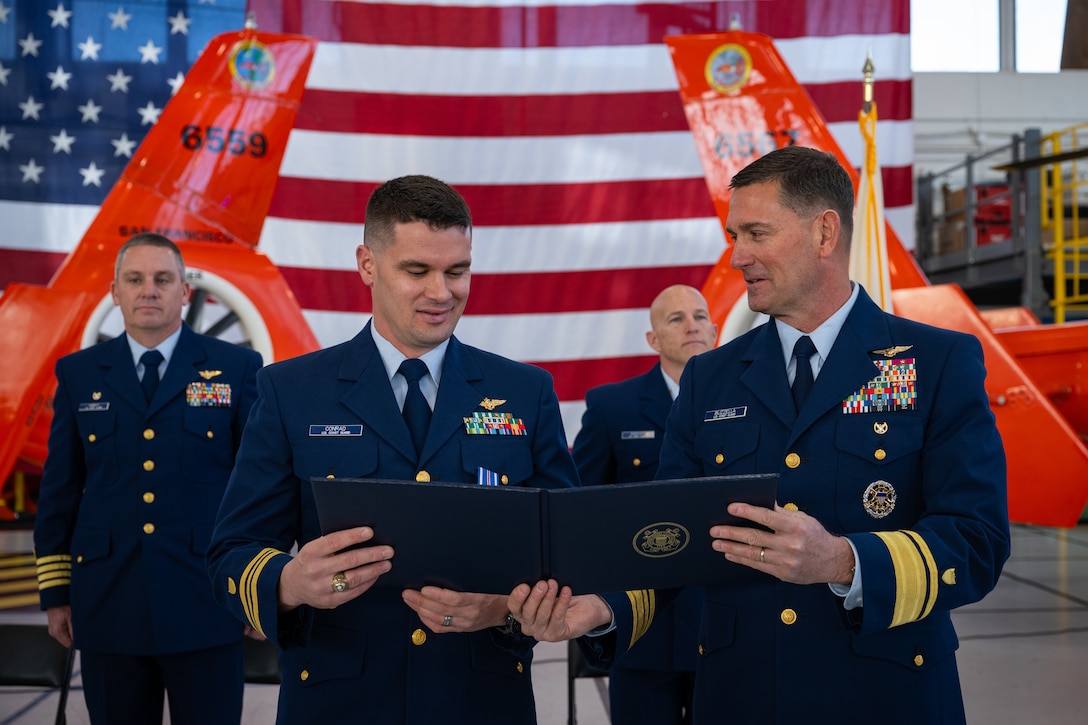 Rear Adm. Joseph Buzzella (right) presents the Distinguished Flying Cross Medal to Lt. Cmdr. Jacob Conrad during an award ceremony at Air Station San Francisco, Dec. 12, 2024. During the ceremony, Lt. Cmdr. Jacob Conrad was awarded the Distinguished Flying Cross Medal for his actions during a search and rescue case, Dec. 29, 2023. (U.S. Coast Guard photo by Petty Officer 3rd Class Hunter Schnabel)