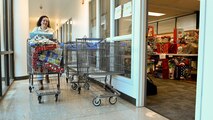 A woman pushed a shopping cart full of wrapped gifts past the doorway of a room full of gifts.