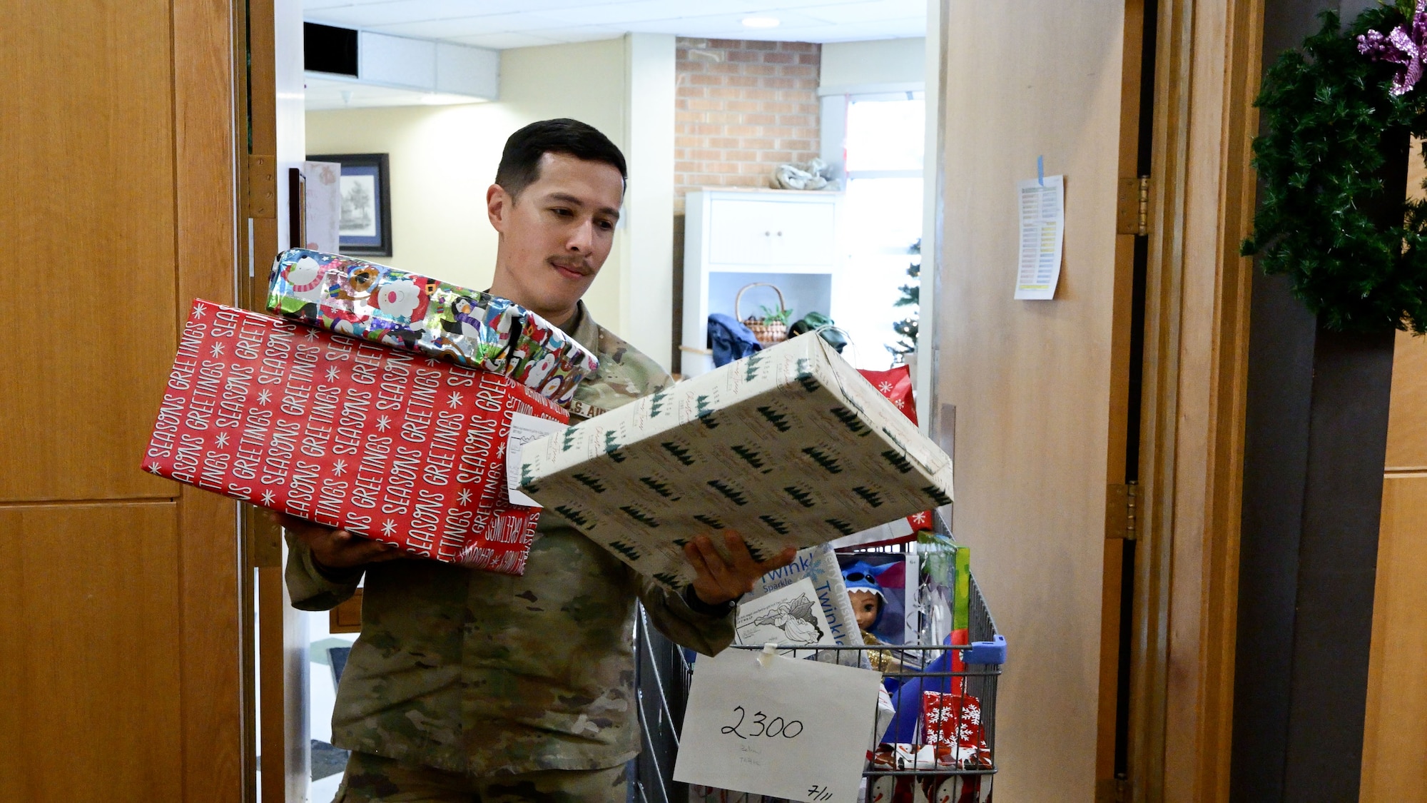 A man in uniform with arms full of gifts looks at a gift tag.