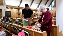 A man and woman inspect wrapped gifts set on pews.