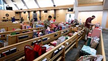 Civilian and military personnel organize wrapped gifts onto church pews in the base chapel.