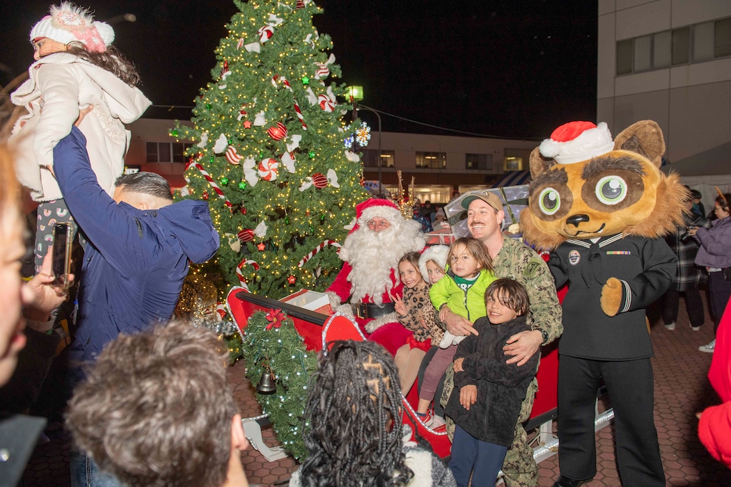 mdr. Patrick Gutierrez, chief staff officer for Commander, Fleet Activities Yokosuka (CFAY), middle, and his family pose for a photo with Santa Claus and CFAY’s mascot Yokopon during a tree lighting ceremony and festival at the installation.