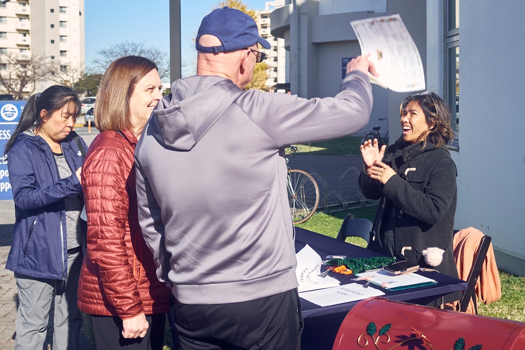 Rodalyn Novak of Commander, Fleet Activities Yokosuka's Fleet and Family Support Center welcomes participants to the CFAY FFSC Volunteer Fair outside the installation's Community Readiness Center December 10, 2024.