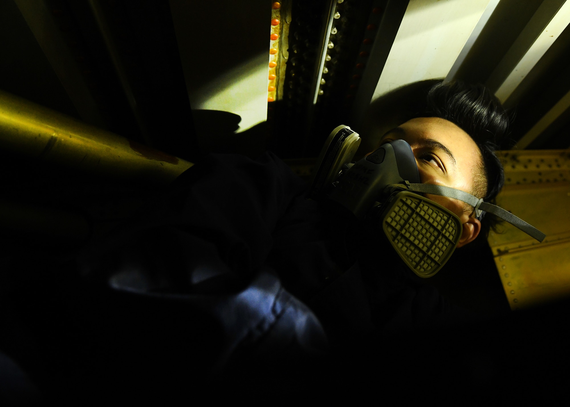 Airman with respirator inside a fuel cell of a wing inspecting seals with a flashlight.