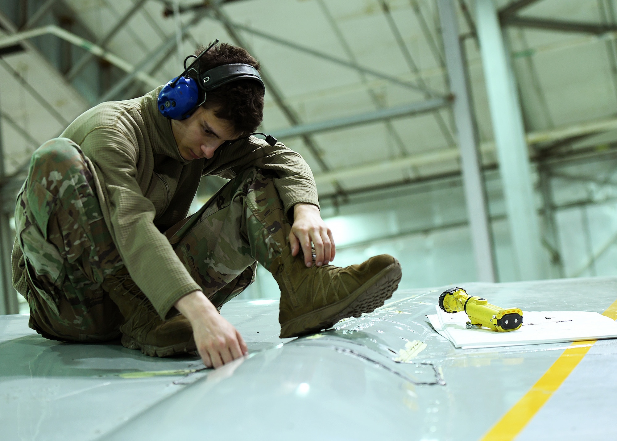 Airman sits on top of an aircraft wing removing a bolt.