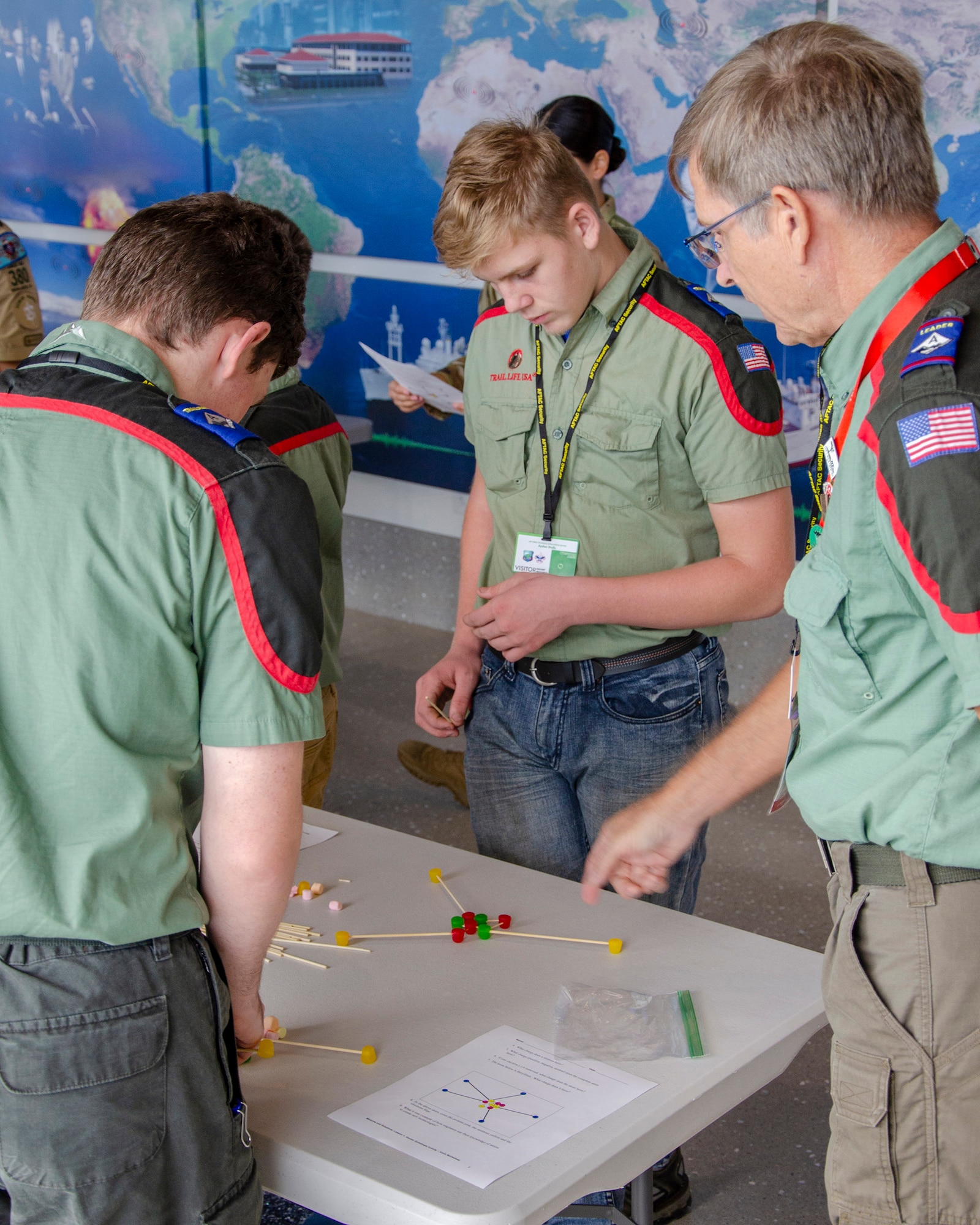 Trailblazers from Trail Life USA take guidance from their advisor, Robert Smith, as they work to construct a 3-D model of an element and its isotopes using candy and toothpicks during the Nuclear Science Merit Badge event hosted by the Air Force Technical Applications Center, Patrick Space Force Base, Fla.  (U.S. Air Force photo by Susan A. Romano)
