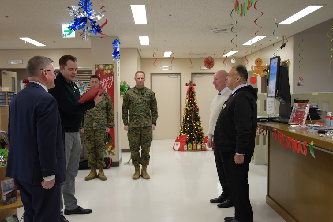 Matthew Schipper, the Camp Fuji Marine Corps Community Services Camp Fuji community services supervisor (second from the left), reads the merits that earned Ceasar Hernandez, the MCCS Camp Fuji Marine and Family Program specialist (far right), a Civilian Service Commendation medal, December 11, 2024.  (U.S. Marine Corps photo by Song Jordan)