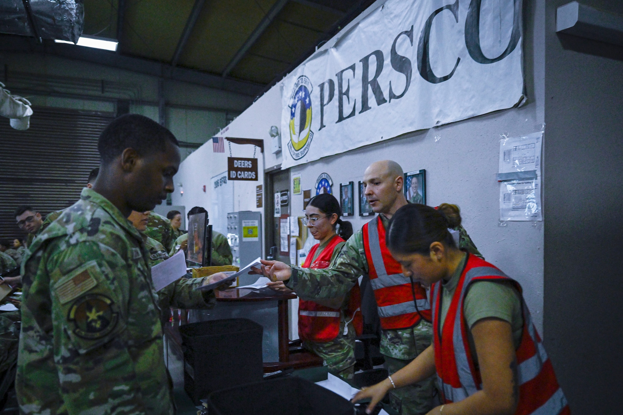 Three military members wearing red vests help a newly arrived Airman in process.