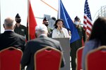 U.S. Ambassador to Albania Yuri Kim speaks from behind a podium with military members and flags behind her