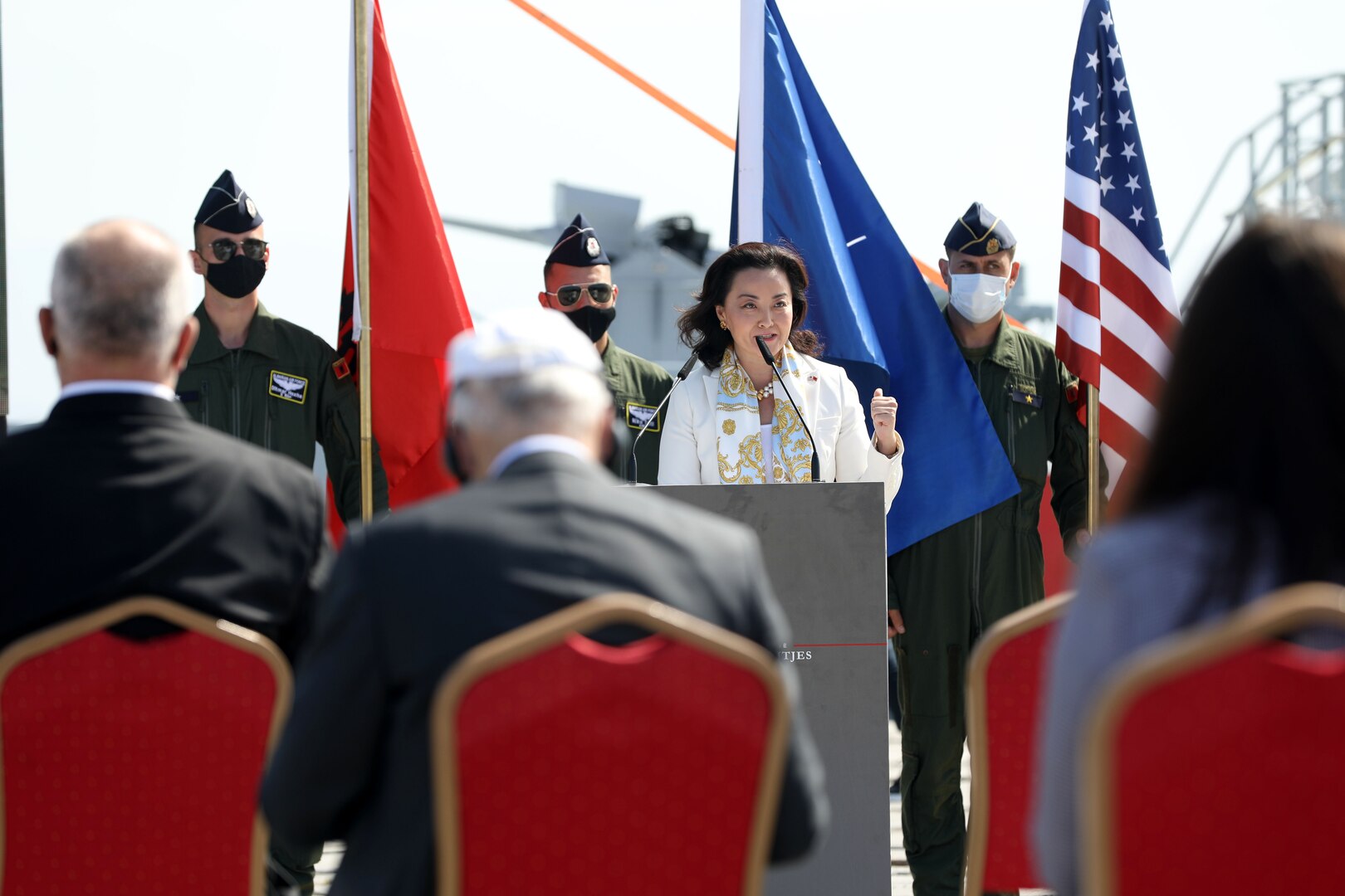 U.S. Ambassador to Albania Yuri Kim speaks from behind a podium with military members and flags behind her