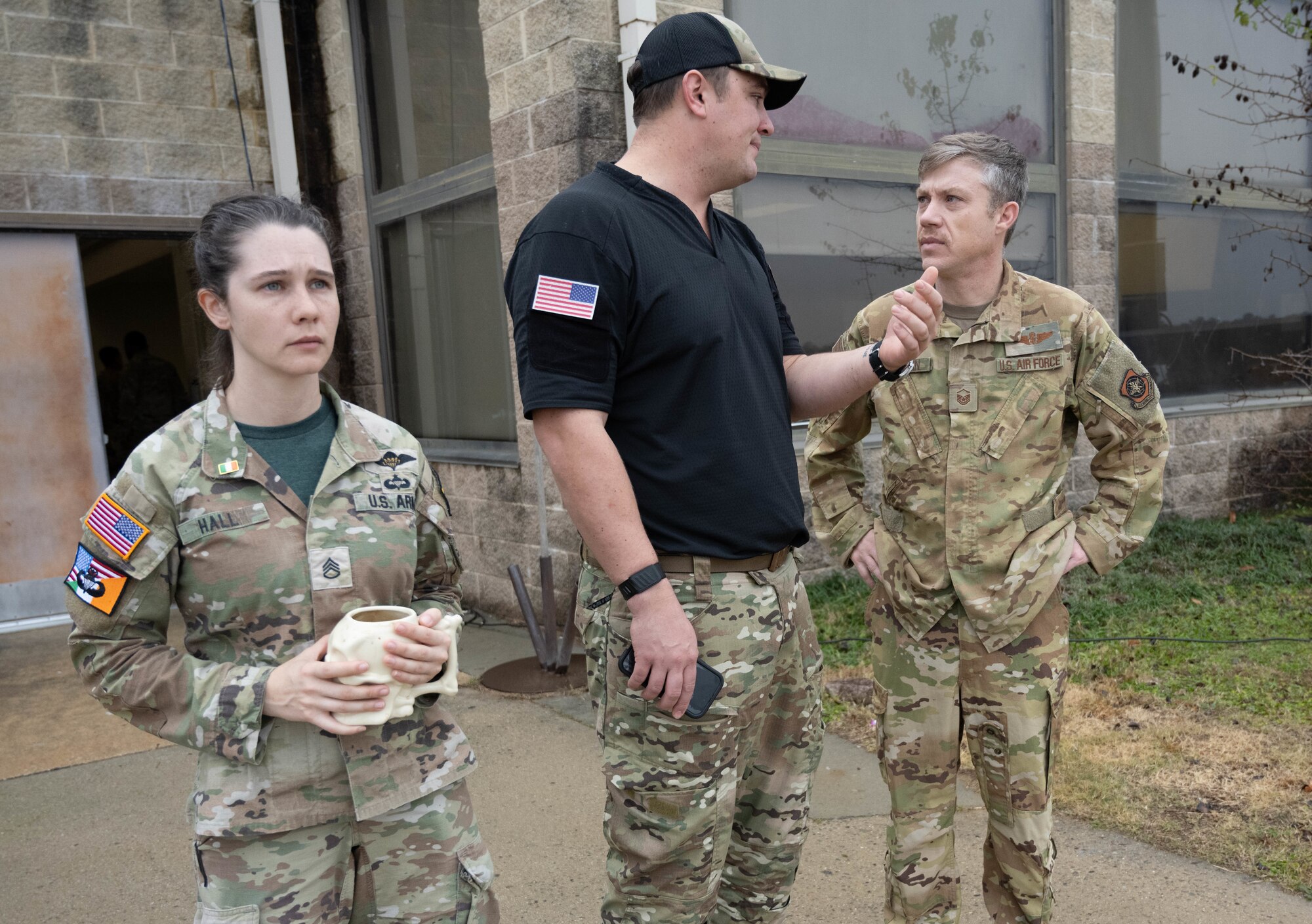 Two soldiers stand with an airmen in front of a passenger terminal.