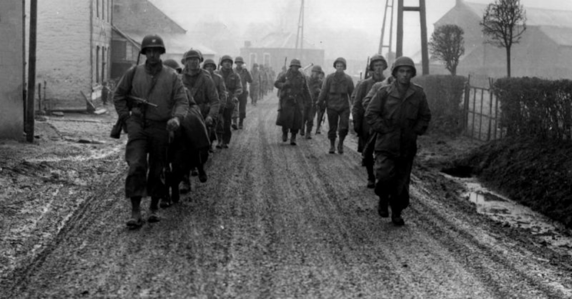 Soldiers of the 28th Infantry Division march down a street in Bastogne, Belgium, in December 1944. Some of these men lost their weapons during the German advance in this area. (U.S. Army photo)