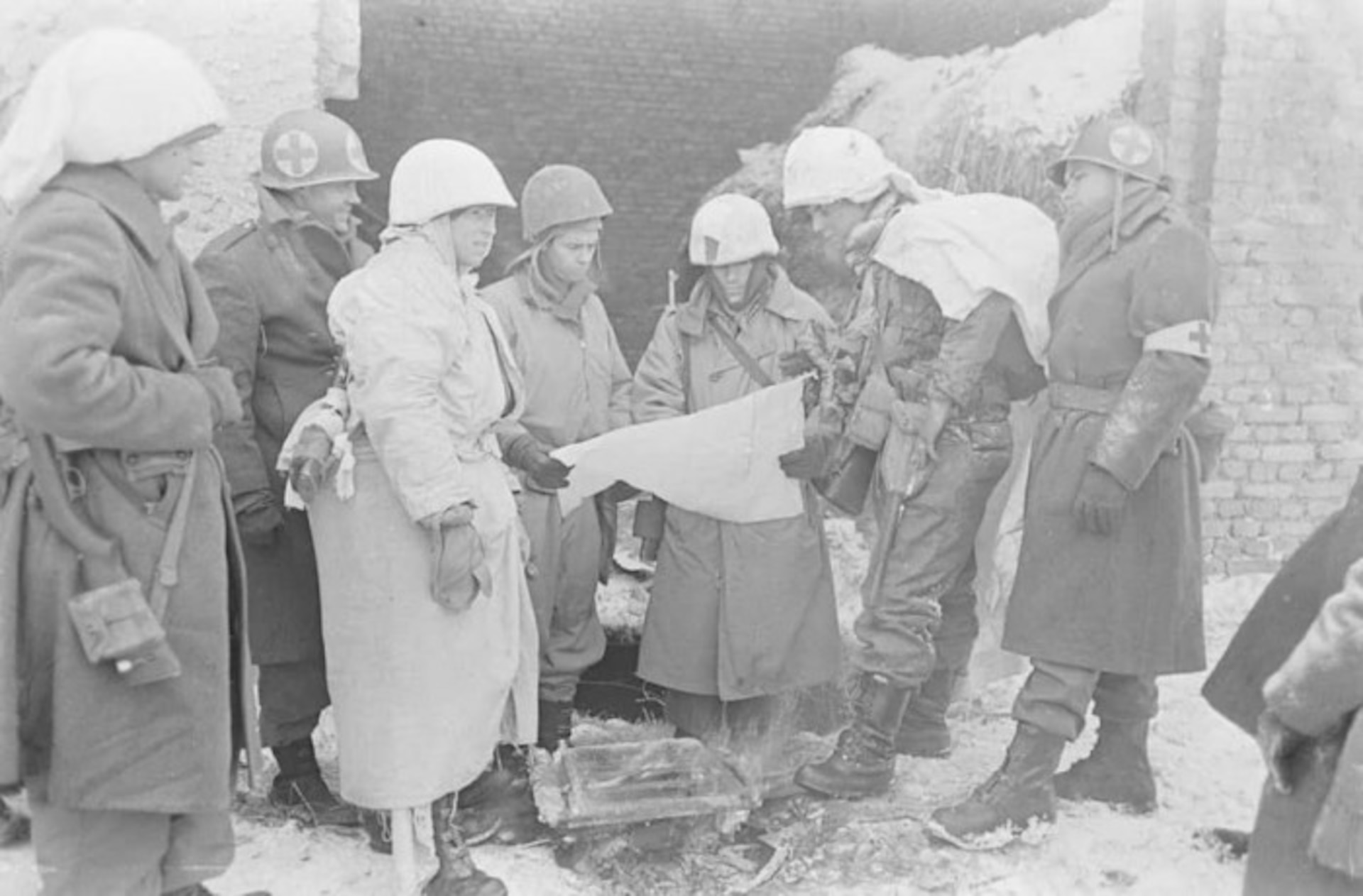 U.S. Army infantrymen with medics in winter uniforms huddled around a map during the Battle of the Bulge. (U.S. Army photo)