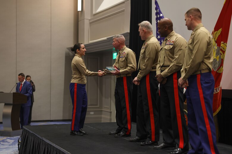 U.S. Marine Corps Capt. Frances Moore, officer selection officer, Officer Selection Team Dallas, 8th Marine Corps District, left, receives an award from U.S. Marine Corps Gen. Eric Smith, 39th Commandant of the Marine Corps, for her achievements throughout Fiscal Year 2024 during the Fiscal Year 2025 National Officer Selection Officer Training Symposium in Orlando on Dec. 11, 2024. NOSOTS is designed to conduct training, discuss recruiting topics and issues and recognize those Officer Selection Teams which have distinguished themselves during the previous fiscal year. (U.S. Marine Corps photo by Lance Cpl. Brenna Ritchie)