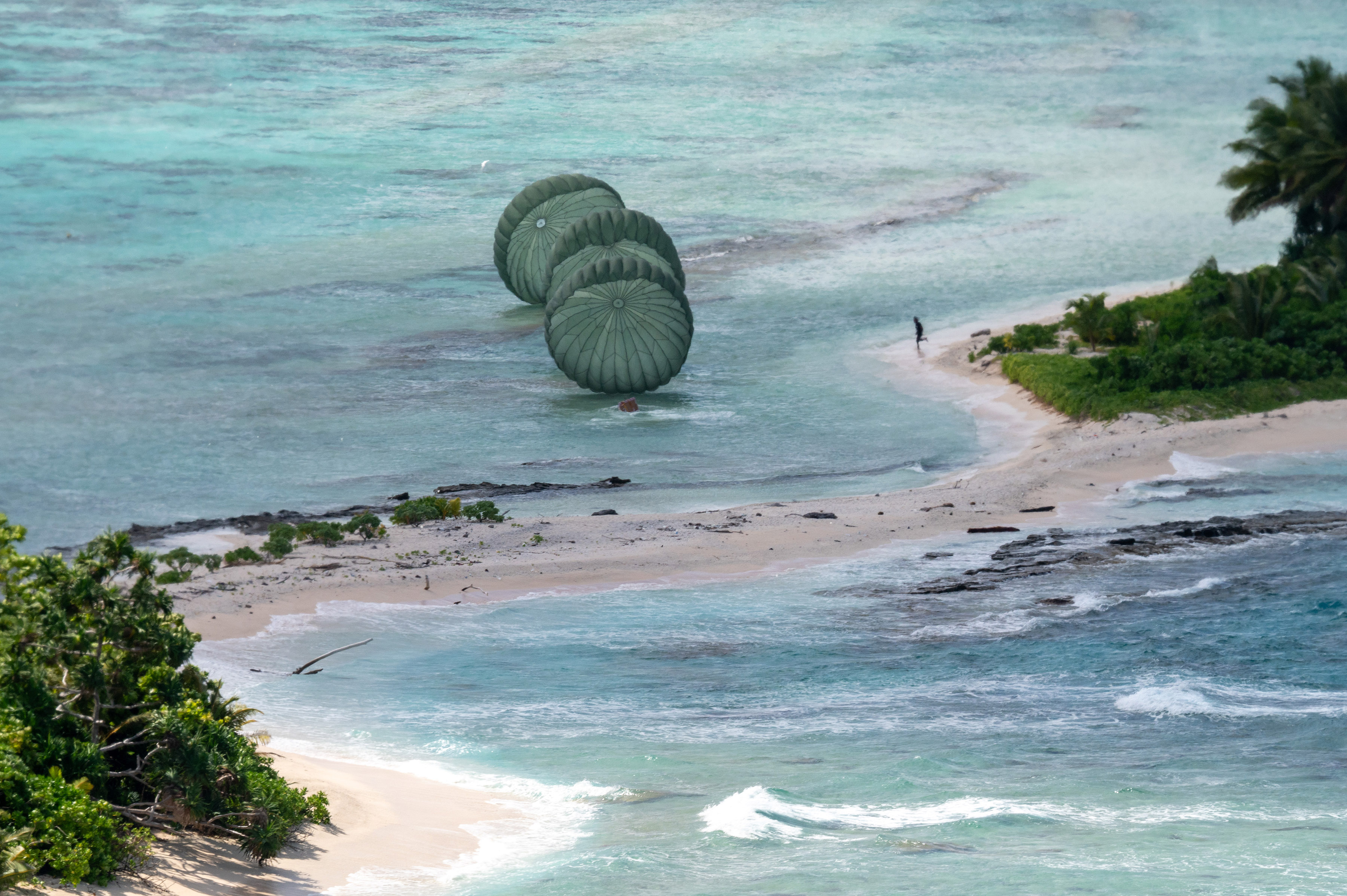 A person on Tamatam, Micronesia, runs to retrieve bundles air-dropped from a U.S. Air Force C-130J Super Hercules aircraft during Operation Christmas Drop, Dec. 12, 2024.