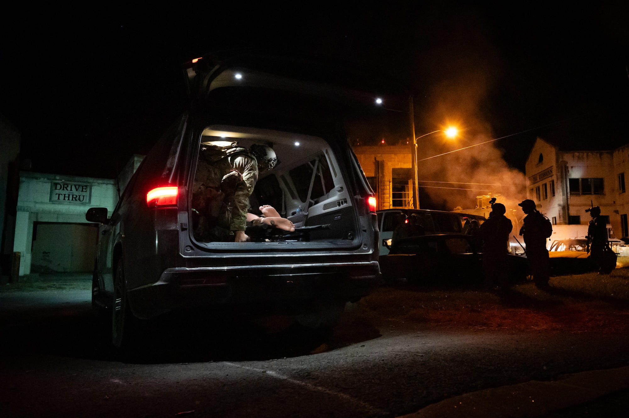 A U.S. Army Green Beret stabalizes a simulated patient in the back of a SUV while other U.S. Army Green Berets and Air National Guard Airmen maintain security in an urban environment.